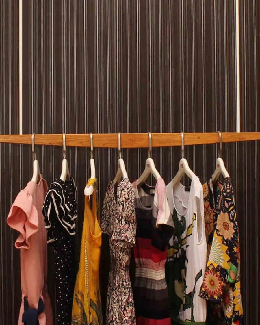 Trendy dresses on hangers against striped background.